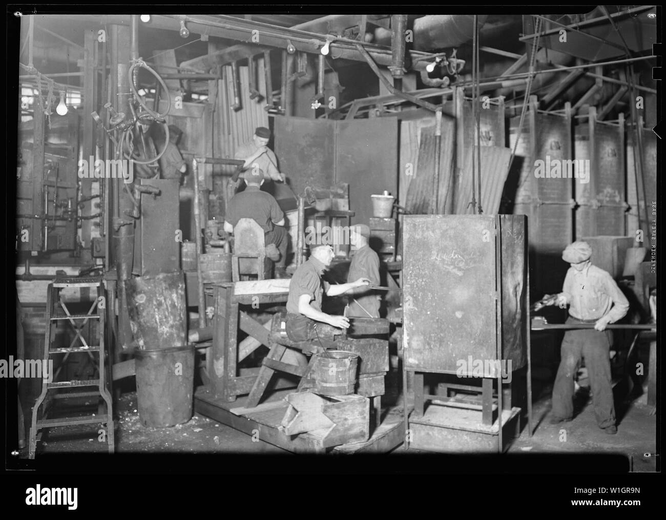 Millville, New Jersey - Glass bottles. Whitall Tatum green glass shop; Scope and content:  Millville, New Jersey - Glass bottles. Whitall Tatum green glass shop. The worker at the extreme left of the picture is a blower taking glass from the oven. To his right is a second blower rolling and blowing the glass on a sheet of iron before he puts it in a mould for final blowing. Under him is sitting the shaping mould boy. The man in profile toward the shaping mould boy is the carrying-up boy who takes the bottles from the mould to the gaffer, who is seated slightly to his left in this picture. The Stock Photo