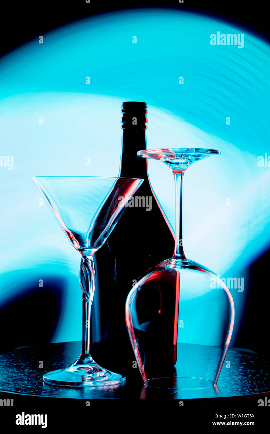 A photo of a wine bottle and two glasses against a light blue stain on a black wall Stock Photo