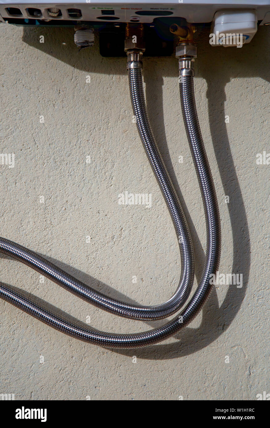 Close-up photography of two propane hoses connected to a gas water heater, casting a shadow on a rough wall. Captured at the Andean mountains of centr Stock Photo