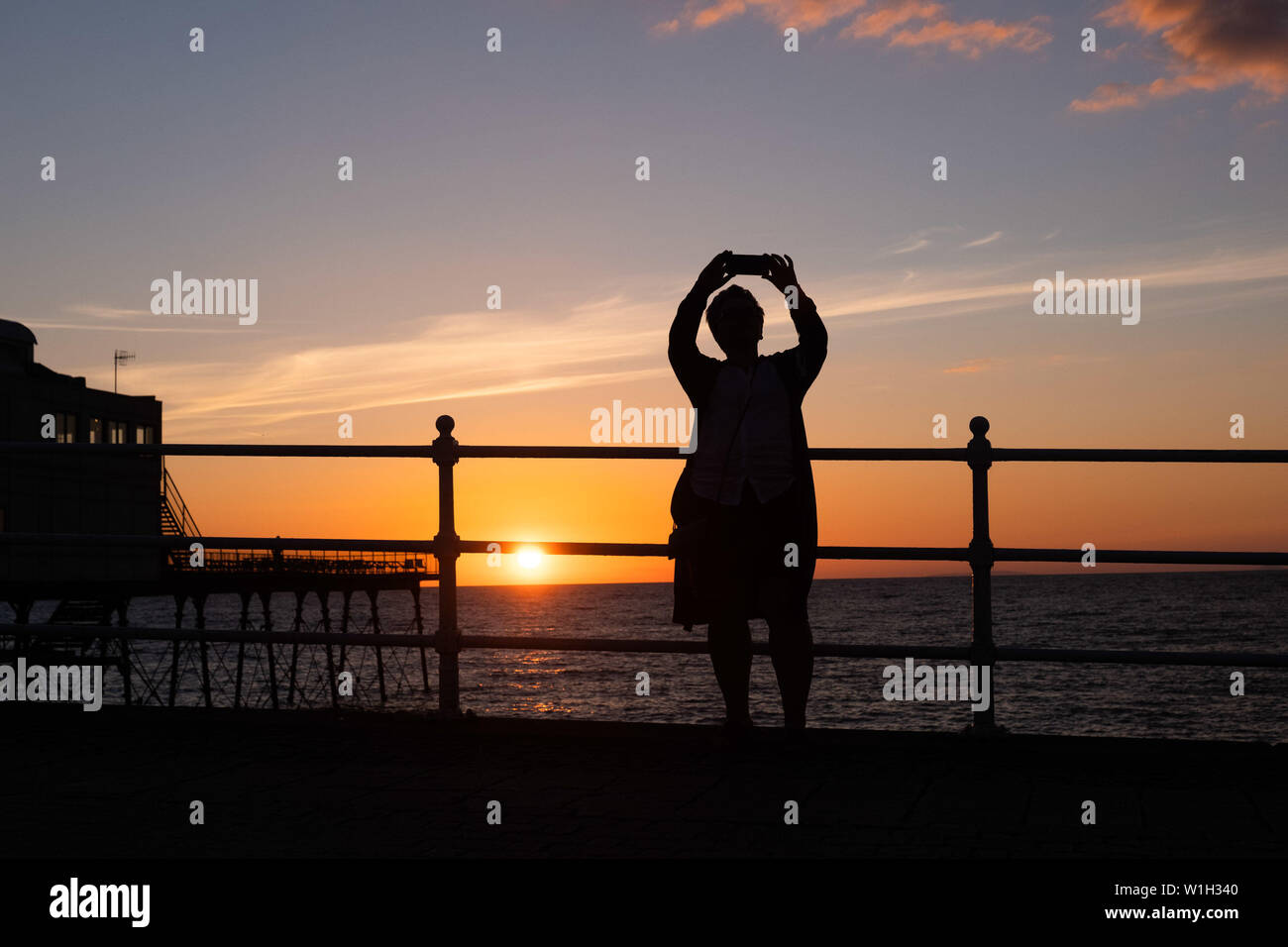 Aberystwyth Wales UK, Tuesday 02 July 2019  UK Weather: A woman takes a selfie, silhouetted against the sky as they watch the glorious sunset in Aberystwyth on the Cardigan Bay coast, west Wales.   photo credit: Keith Morris//Alamy Live News Stock Photo