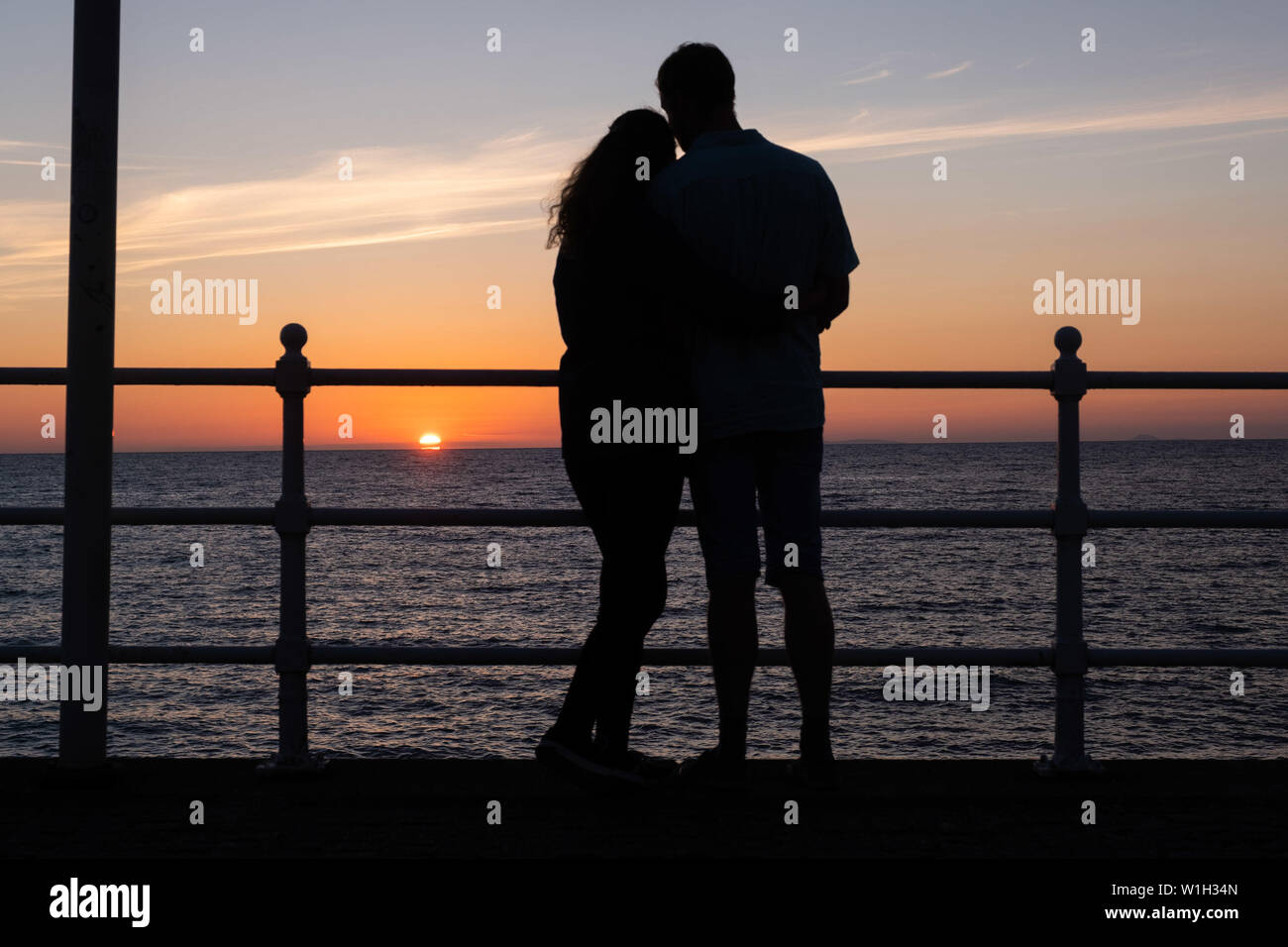 Aberystwyth Wales UK, Tuesday 02 July 2019  UK Weather: A couple embrace, silhouetted against the sky as they watch the glorious sunset in Aberystwyth on the Cardigan Bay coast, west Wales.   photo credit: Keith Morris//Alamy Live News Stock Photo