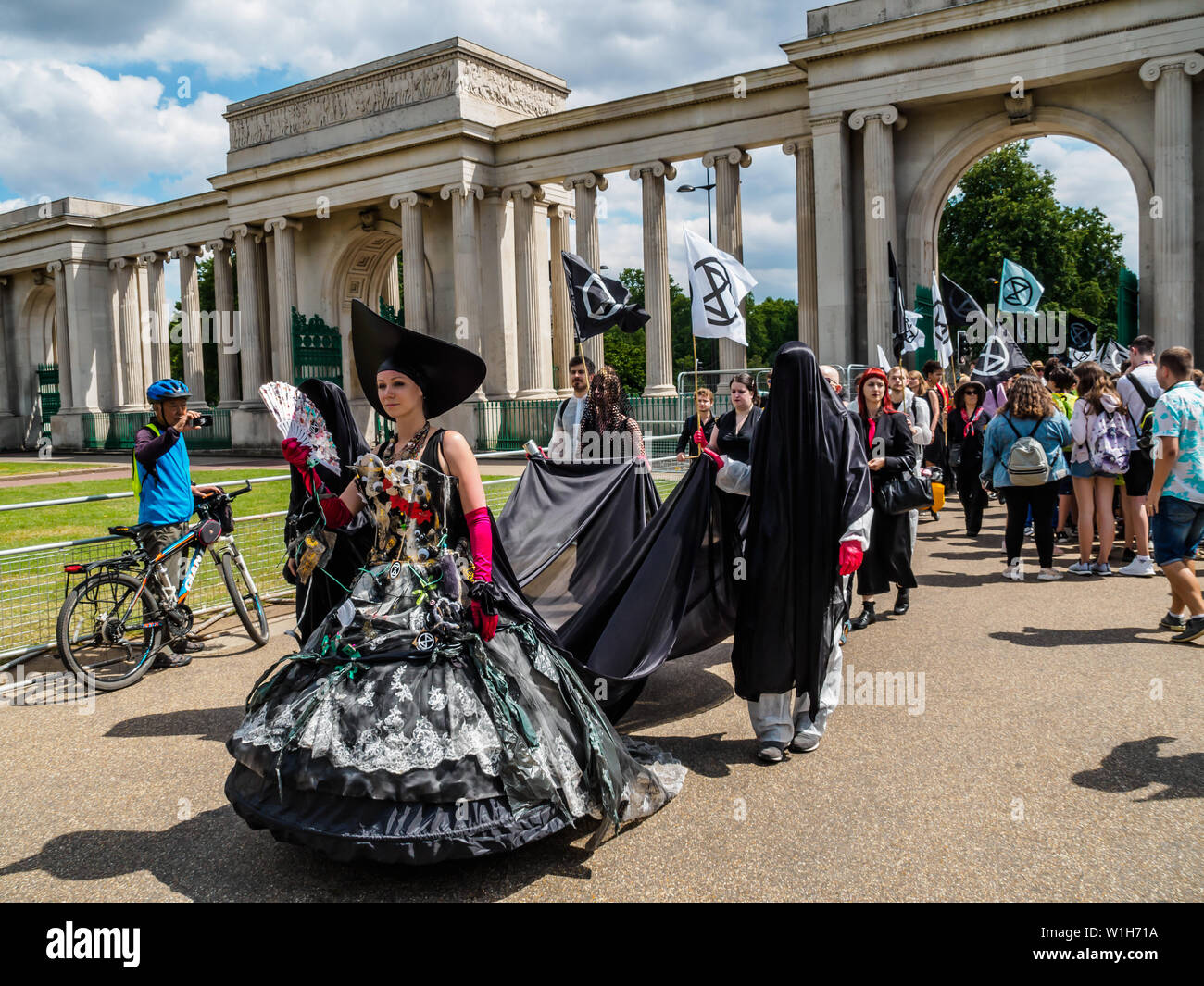 London, UK. 2nd July 2019. A procession by Extinction Rebellion walks past Hyde Park Corner on its way to perform outside offices oil companies in the Oil and Gas Climate Initiative (OGCI) urging them to abandon the pretence they can combat global warming without a huge cut in oil production. The protest on the day that BP were sponsoring a Royal Opera House performance of Carmen to be relayed to 13 BP big screens starred Carmen speaking, a fine opera singer and XR drummers and a team marking the companies as crime scenes. Peter Marshall/Alamy Live News Stock Photo