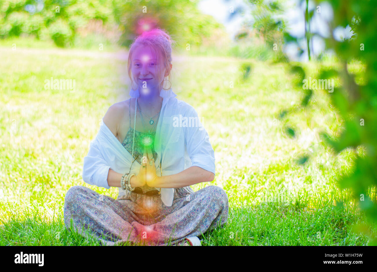 Happy woman is meditating in the lotus pose with glowing seven chakras ...
