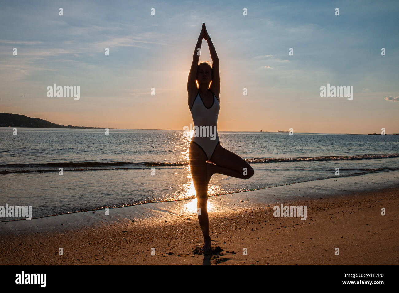 Silhouette woman yoga on the beach at sunset. Woman is practicing yoga at sunset on sea coast. Calm and self control. Stock Photo