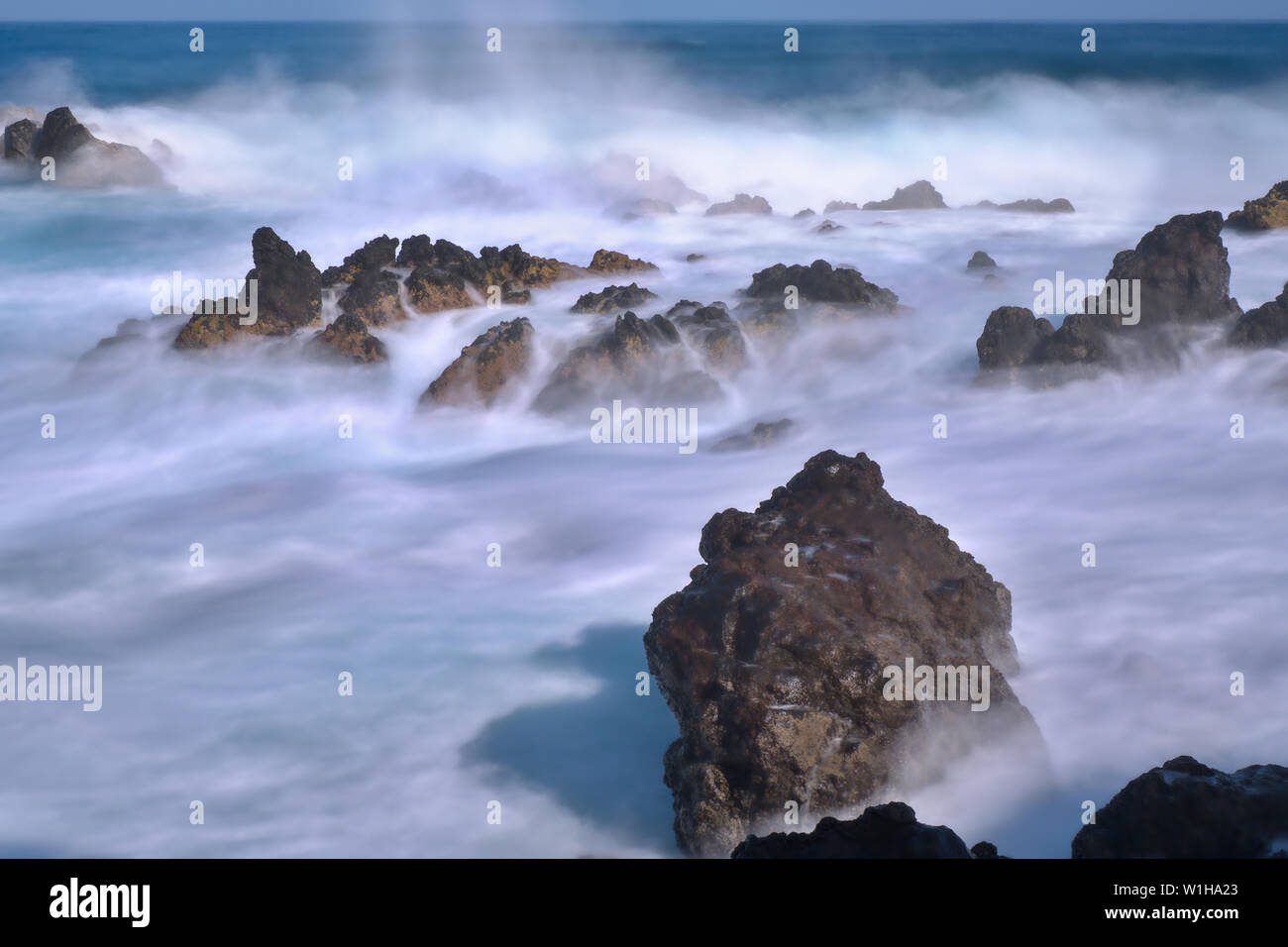 Excerpt from the Atlantic Ocean on teneriffa with waves and spray over black lava stones. Long exposure photography with ND filter, the water is misty Stock Photo