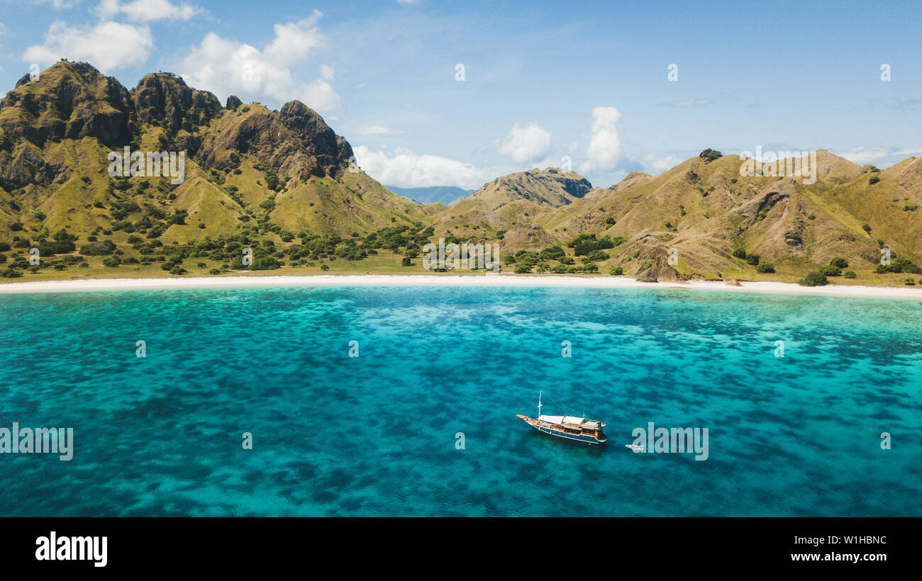 Luxury cruise boat sailing over coral reef with amazing tropical beach and mountain view. Aerial view. Padar island, Komodo Indonesia. Stock Photo