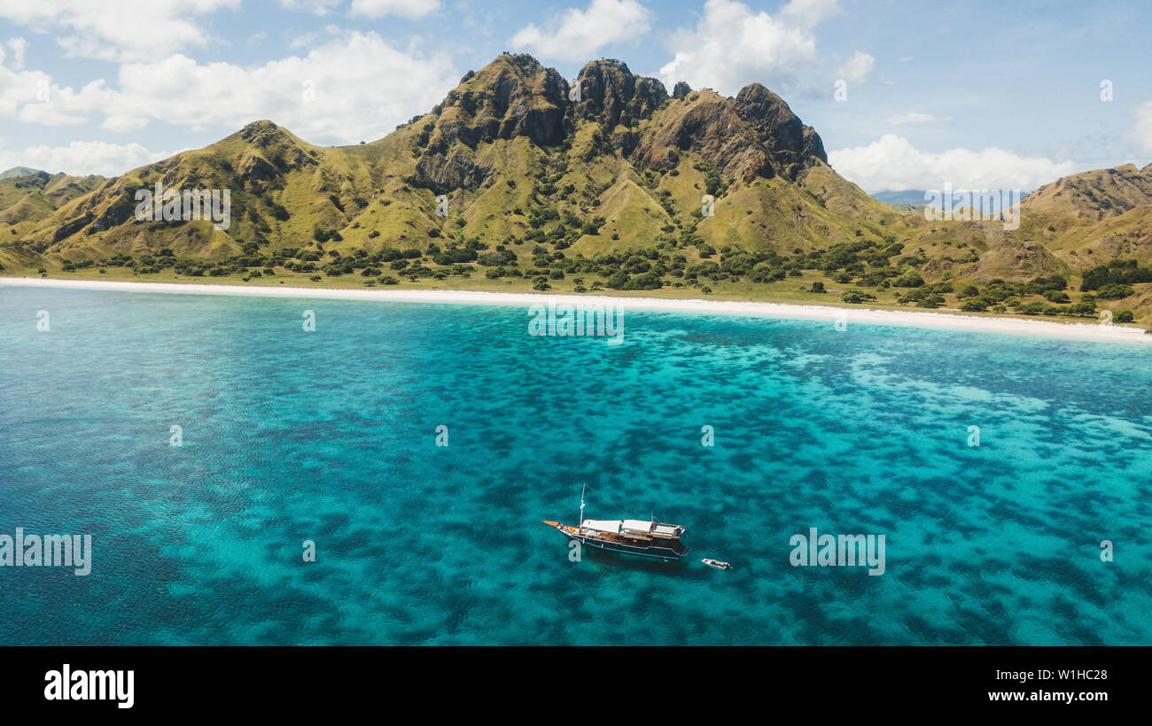 Luxury cruise boat sailing over coral reef with amazing tropical beach and mountain view. Aerial view. Padar island, Komodo Indonesia. Stock Photo