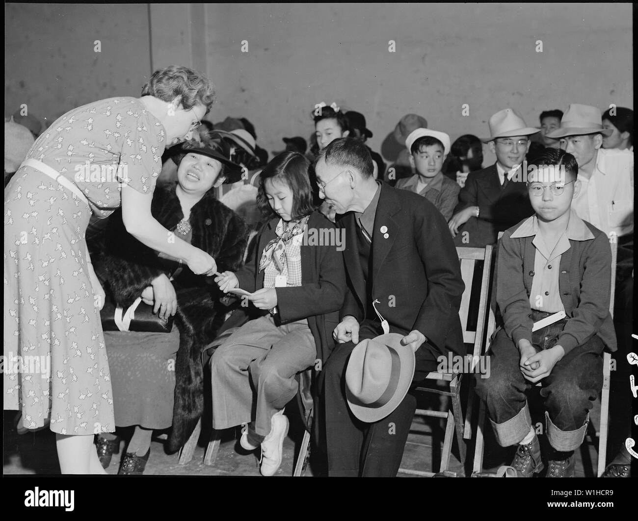 Oakland, California. Mr. and Mrs. Kitagaki with two of their children at the Wartime Civil Control . . .; Scope and content:  The full caption for this photograph reads: Oakland, California. Mr. and Mrs. Kitagaki with two of their children at the Wartime Civil Control Administration station a few minutes before departure by bus for Tanforan Assembly center. A local church member is handing Kimiko a pamphlet expressing the good wishes of the church toward the departing evacuees. Mr. Kitagaki, prior to evacuation, was in the cleaning and dyeing business. Stock Photo
