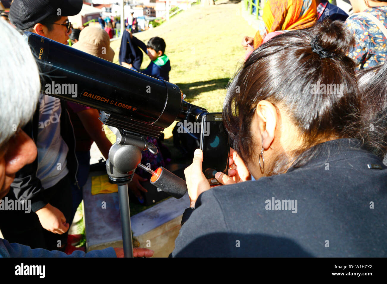 La Paz, Bolivia 2nd July 2019: A woman takes a photo of a partial eclipse of the sun using her mobile phone over a telescope eyepiece at an eclipse watching event near the city centre. In La Paz the eclipse lasted for about 2 hours 10 minutes with about 55% coverage at its maximum. Stock Photo