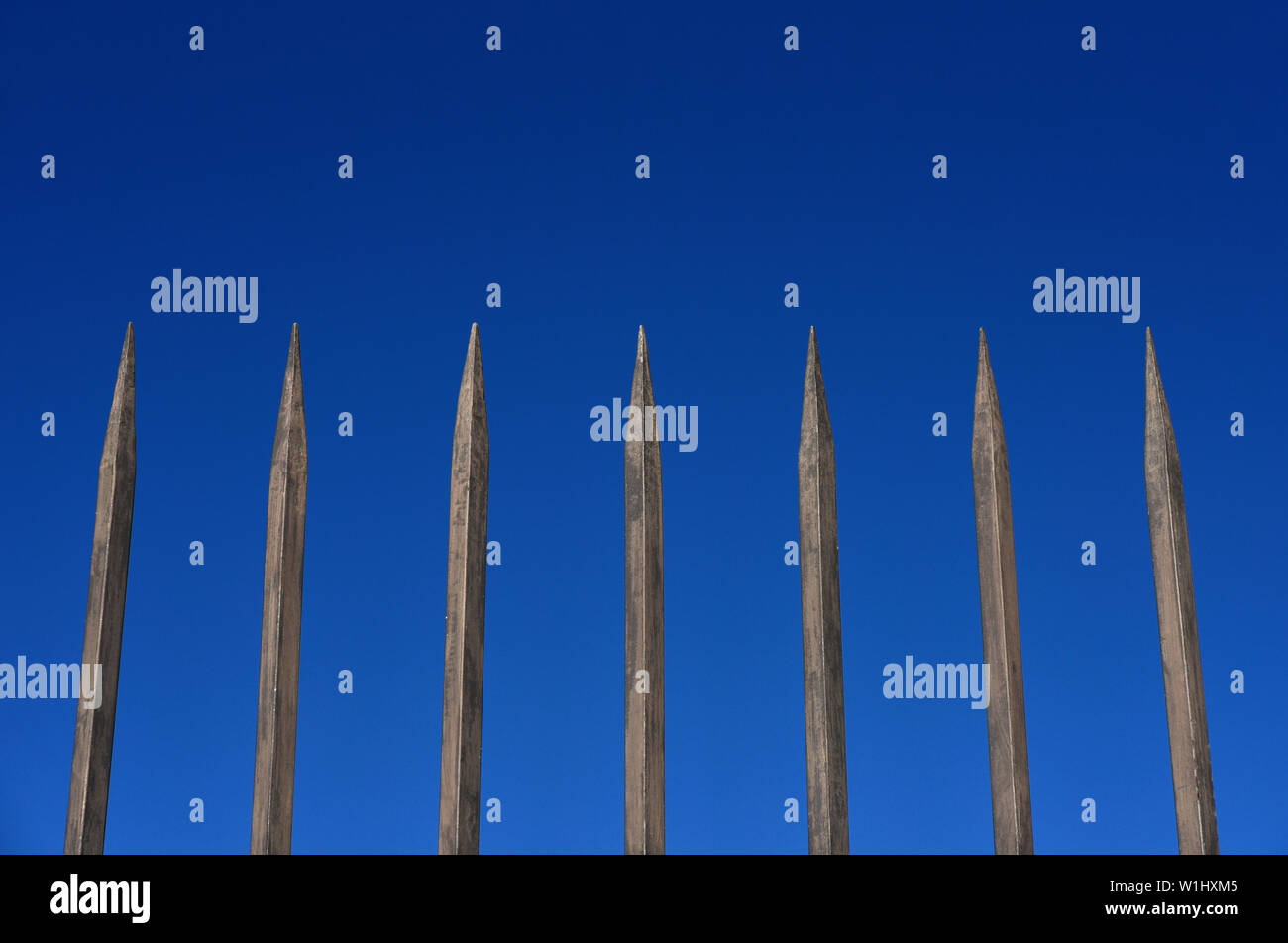 Steel fence barrier with pointed bars against blue sky. Concept of reclusion, obstacle, secutiry of protection Stock Photo