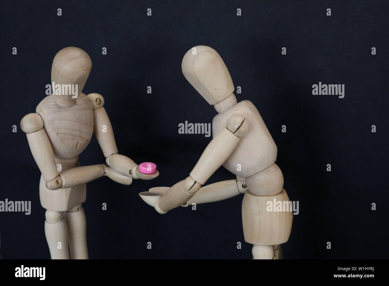 2 wooden mannequins one accepting a pink pill tablet drug from the other. Illegal prescription drug taking choice decision concept. drug education awa Stock Photo