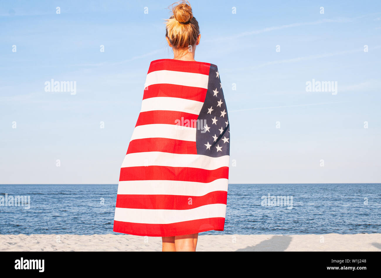 Beautiful patriotic woman with American flag on the beach. USA Independence day, 4th July. Freedom concept, view from the back. Stock Photo