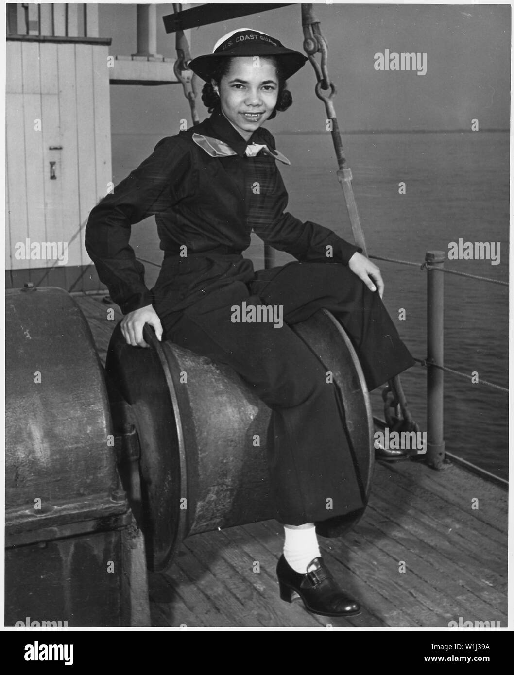 SPAR Aileen Anita Cooke, a prentice seamen, is receiving her boot course at a United States Training Station, Manhattan Beach, Brooklyn, New York; Scope and content:  SPAR Aileen Anita Cooke, apprentice seamen, is receiving her boot course at a United States Training Station, Manhattan Beach, Brooklyn, New York. She is shown seated on a winch on the deck of the dry-land training ship USS Neversail. Seaman Cooke enlisted in the United States Coast Guard Women's Reserve in February. The daughter or Mr. and Mrs. Allan A. Vooke of 1141 East 58th Street, Los Angeles, California, she was valedictori Stock Photo