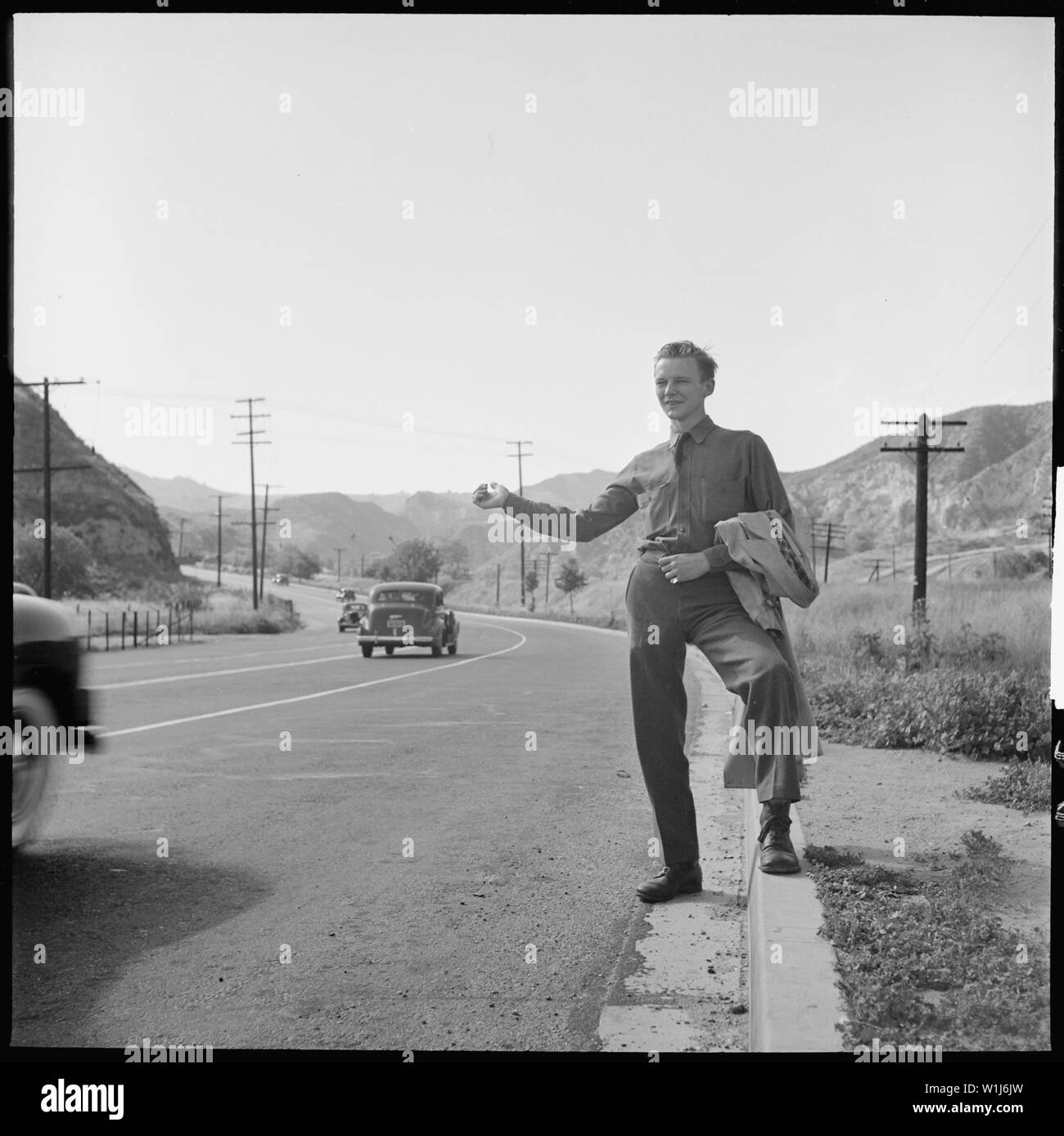 San Fernando, California. Hitch-hiking. This Civilian Conservation Corps boy is returning to camp about thirty miles away after a weekend visit to his family in Los Angeles.; General notes:  — Near Newhall Pass (Ridge Route of Hwy 99) in Sylmar, at the Santa Susana Mountains in the northern San Fernando Valley, Los Angeles, California (1940). Stock Photo