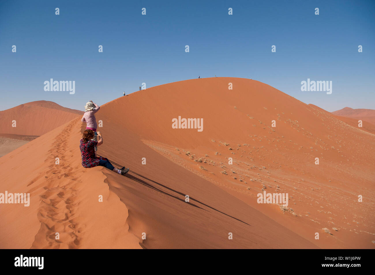 Hikers climbing up a sand dune ridge at Sossusvlei, Namib-Naukluft National Park, Namibia. Stock Photo