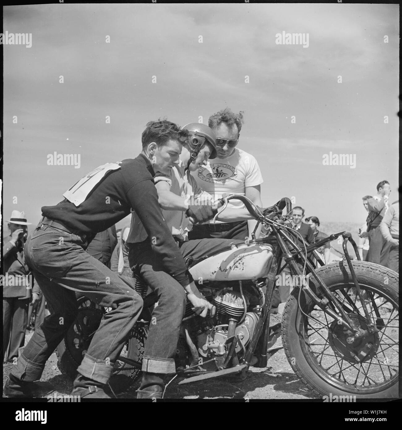 Santa Clara County, California. Motorcycle and Hill Climb Recreation. His first hill climb. The fellow on the left is fiixing the gear shift for him while the other is explaining how to take the bumps. The man with the goggles is wearing a shirt of a local motorcycle club Stock Photo