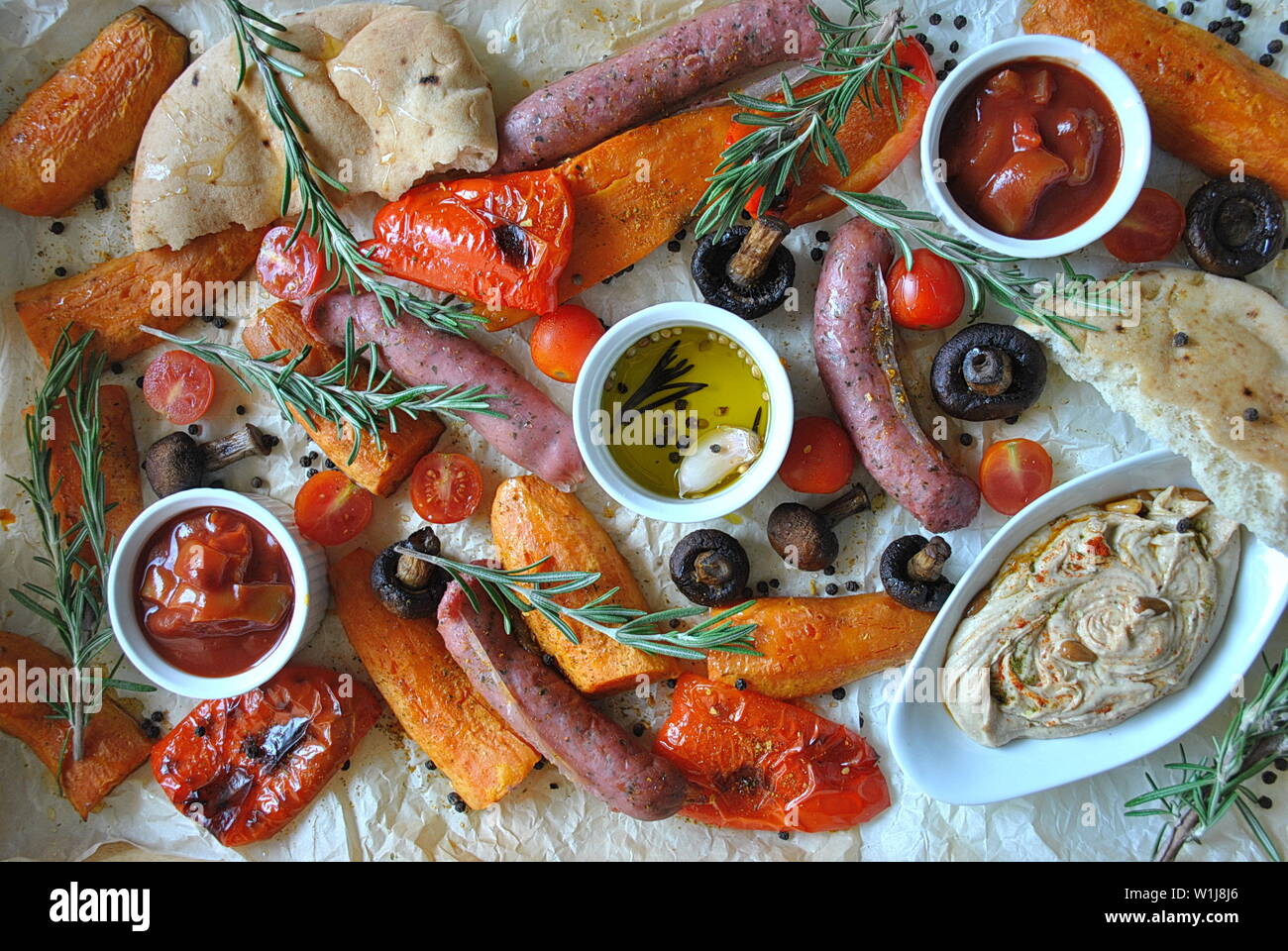 Grilled sausages and vegetables platter served with humus and pita bread, grilled mushrooms, cherry tomatoes, sweet potatoes and herbs. Barbecue grill Stock Photo
