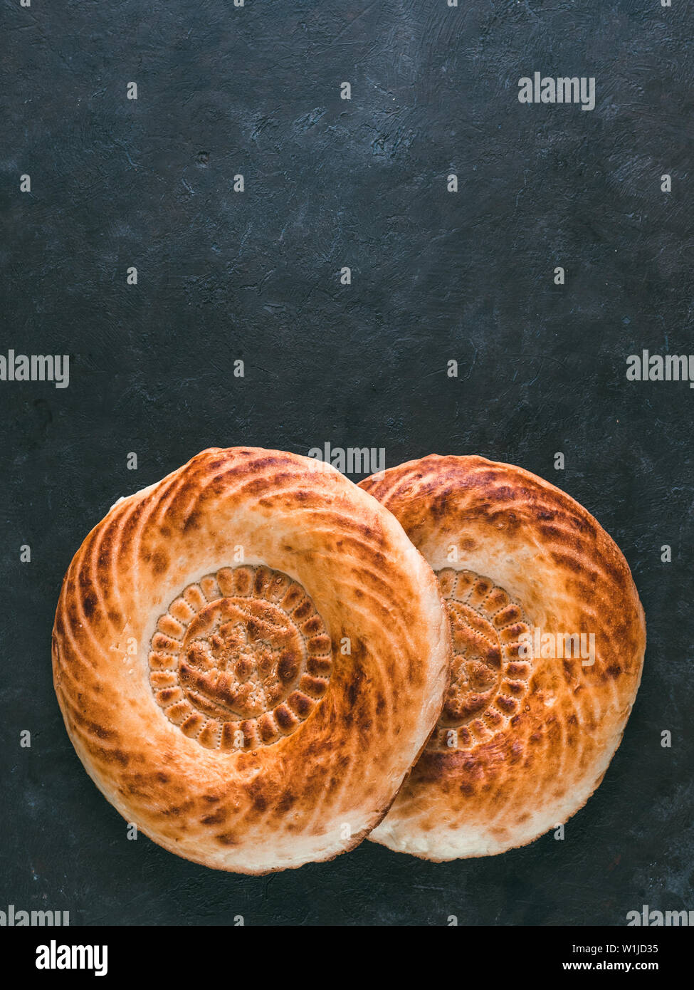 Tasty fresh tandoor bread on black table. Two tandoor flat bread cake on dark stone background. National asian meal and food. Copy space for text. Top view or flat lay. Vertical. Stock Photo