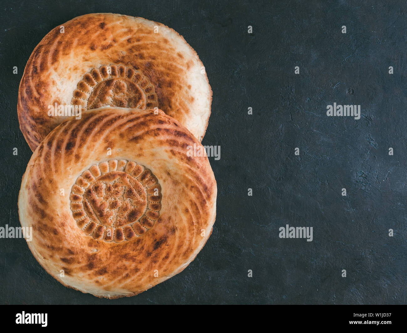 Tasty fresh tandoor bread on black table. Two tandoor flat bread cake on dark stone background. National asian meal and food. Copy space for text. Top view or flat lay. Stock Photo