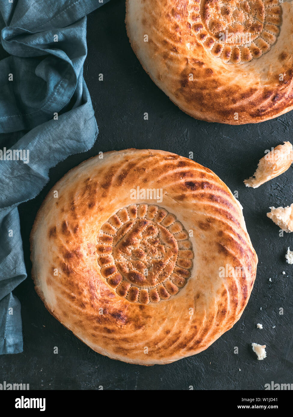 Tasty fresh tandoor bread on black table. Two tandoor flat bread cake with pieces and crumbs on dark stone background. National asian meal and food. Copy space for text. Top view or flat lay. Vertical Stock Photo