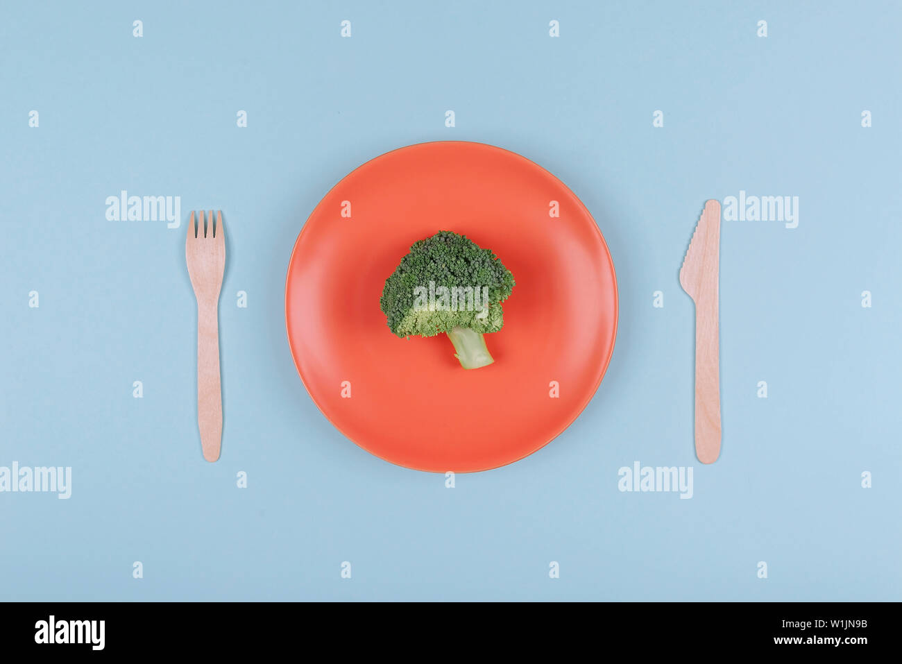 Small piece of fresh broccoli on orange plate with wooden fork and knife. Top view. Stock Photo