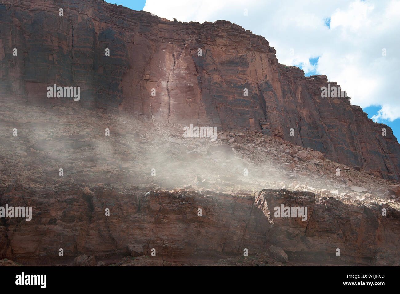 Dust billows from a mountainside moments after a huge slab of sandstone breaks away from a cliff wall high above the Colorado River on Utah State Rout Stock Photo