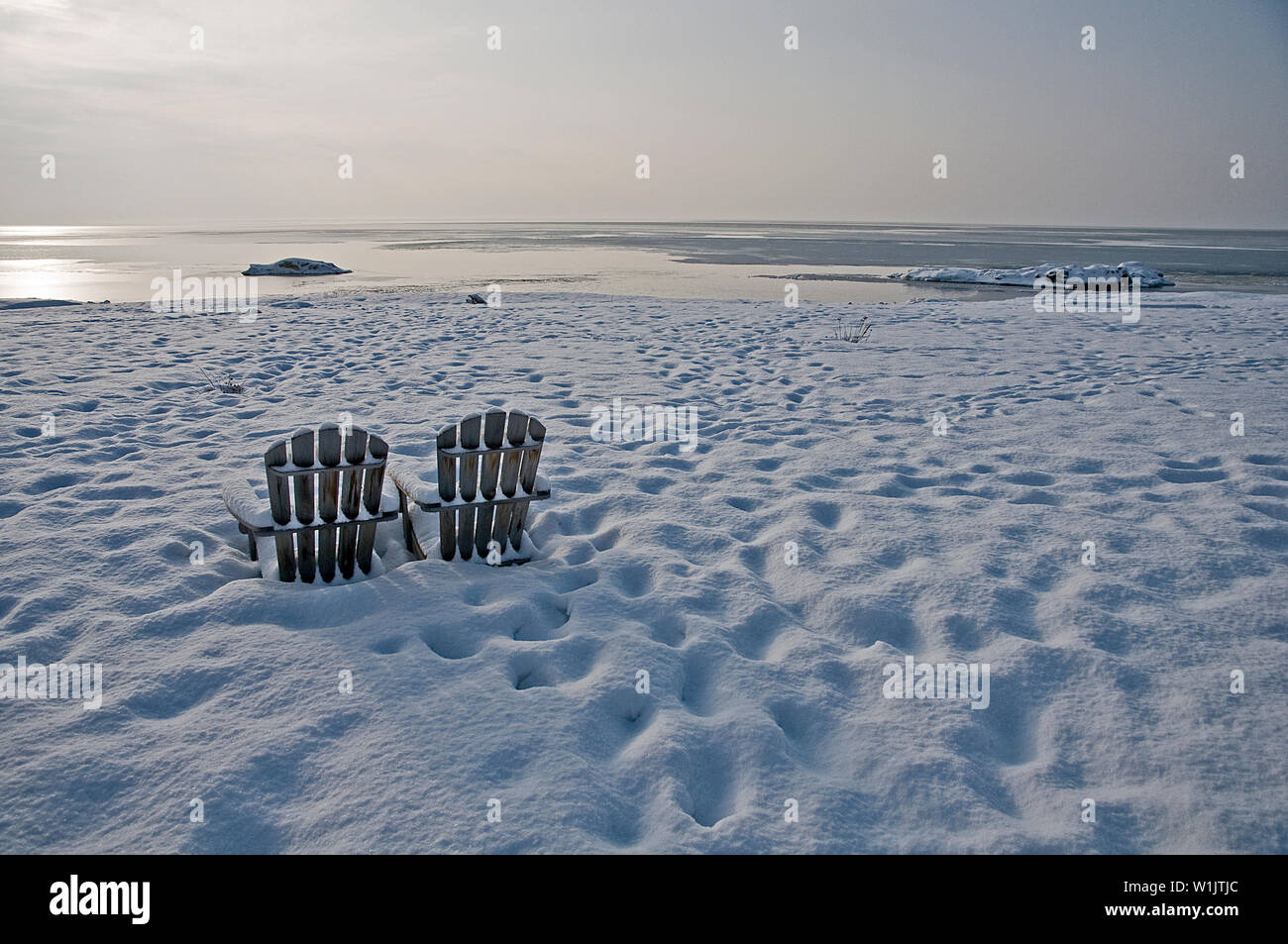 Two Beach Chairs Sit Lonely On A Snow Covered Rock Beach On