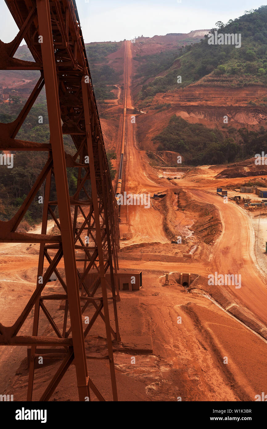 Mining operations for transporting and managing iron ore. From process plant looking up and beneath ore conveyor to primary crusher in far distance Stock Photo