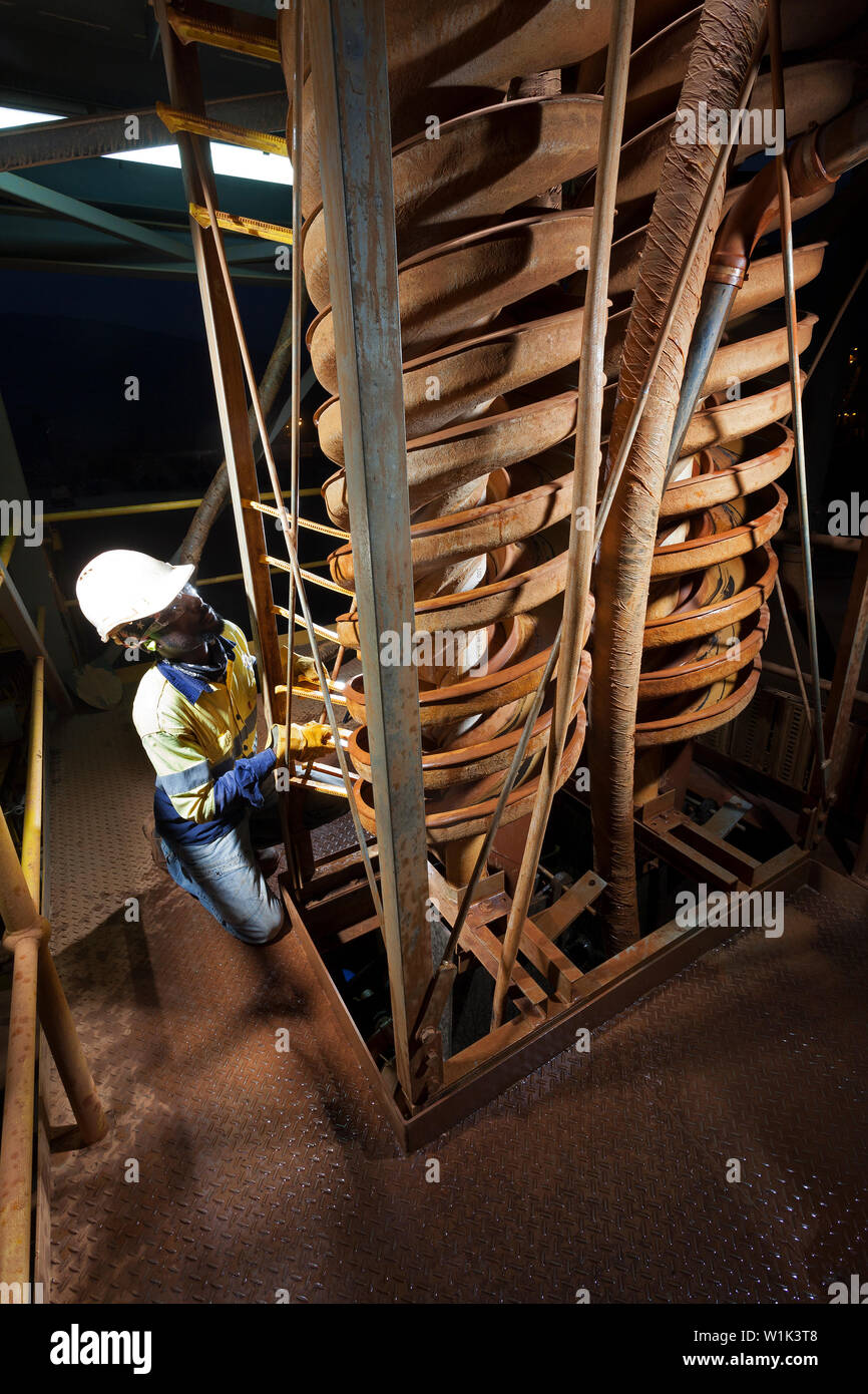 Mining operations for transporting and managing iron ore. Interior of saprolite test plant at dawn & operator adjusting spiral on cyclone concentrator Stock Photo