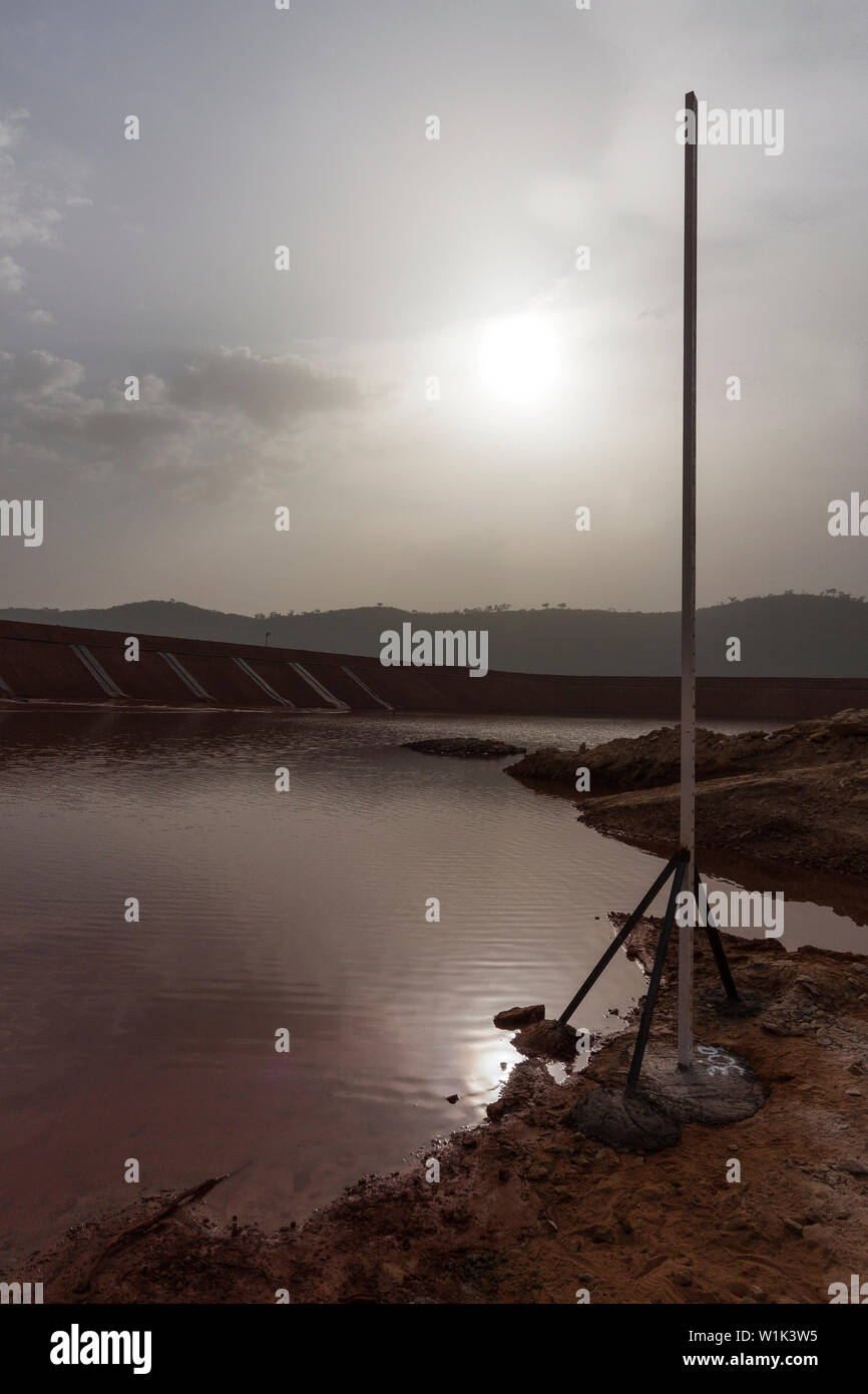 Mining operations for transporting and managing iron ore. Construction of dam wall for tailings storage facility and water effects into sun. Stock Photo