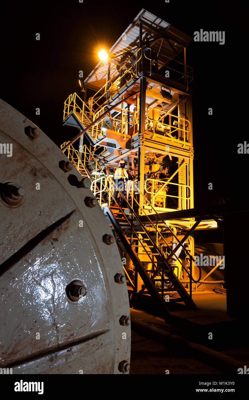 Mining operations for transporting & managing iron ore. Interior of saprolite test plant at dawn & operator adjusting spiral on cyclone concentrator. Stock Photo