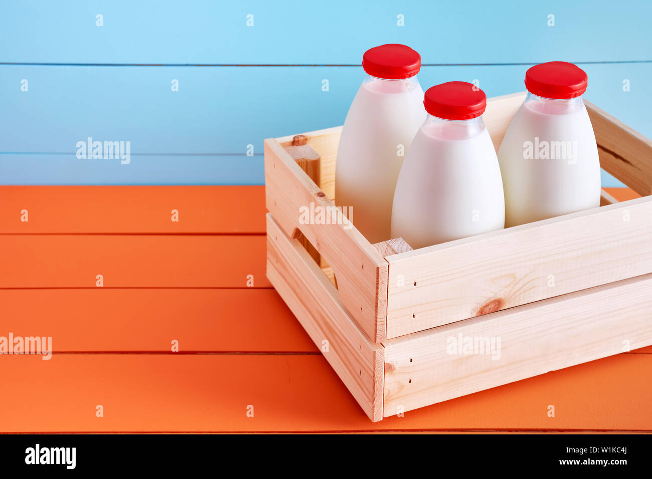 Three milk bottles in a wooden crate on wooden kitchen table with blue