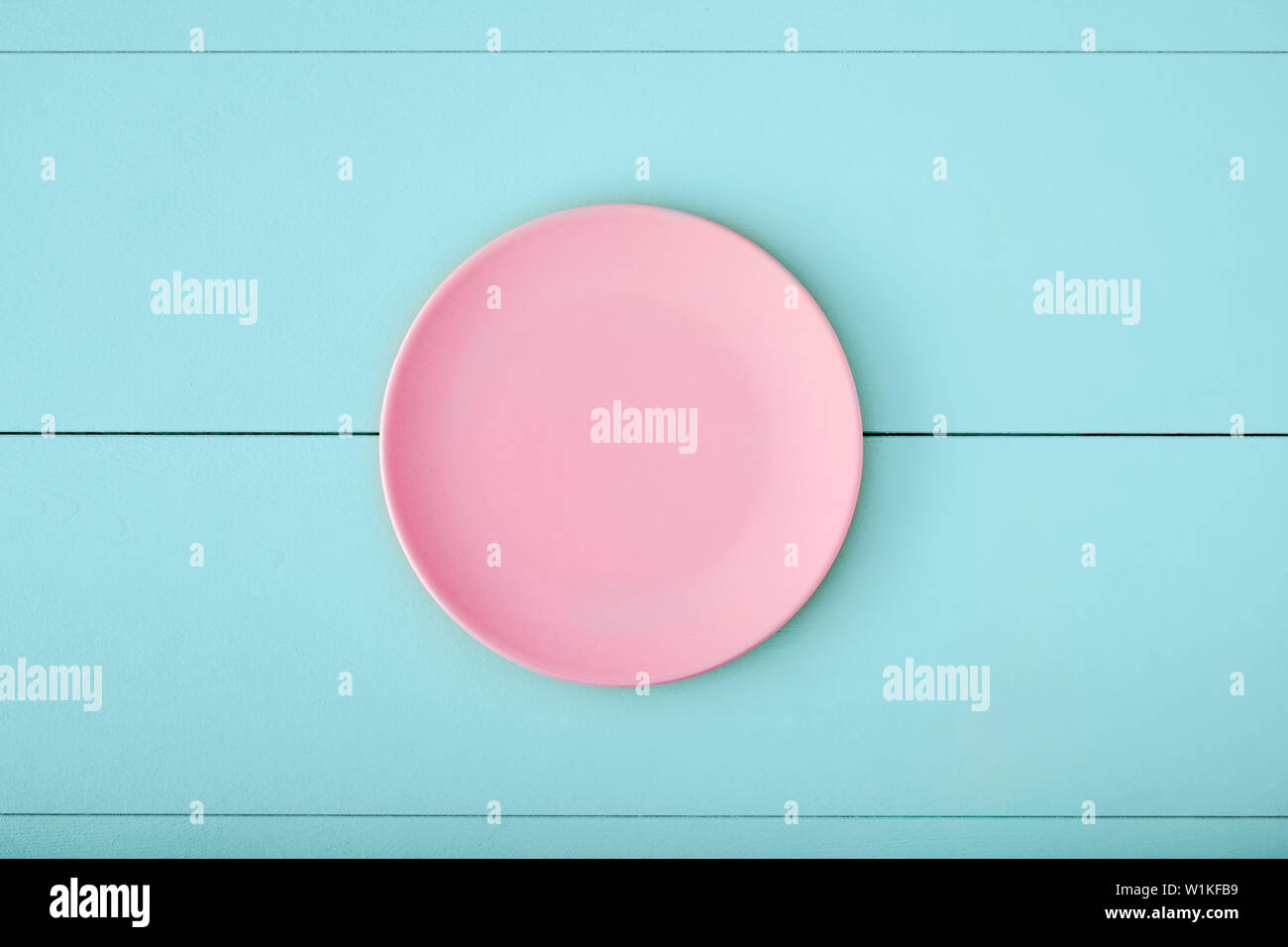 Pink empty plate on turquoise wooden table. Top down view with copy ...