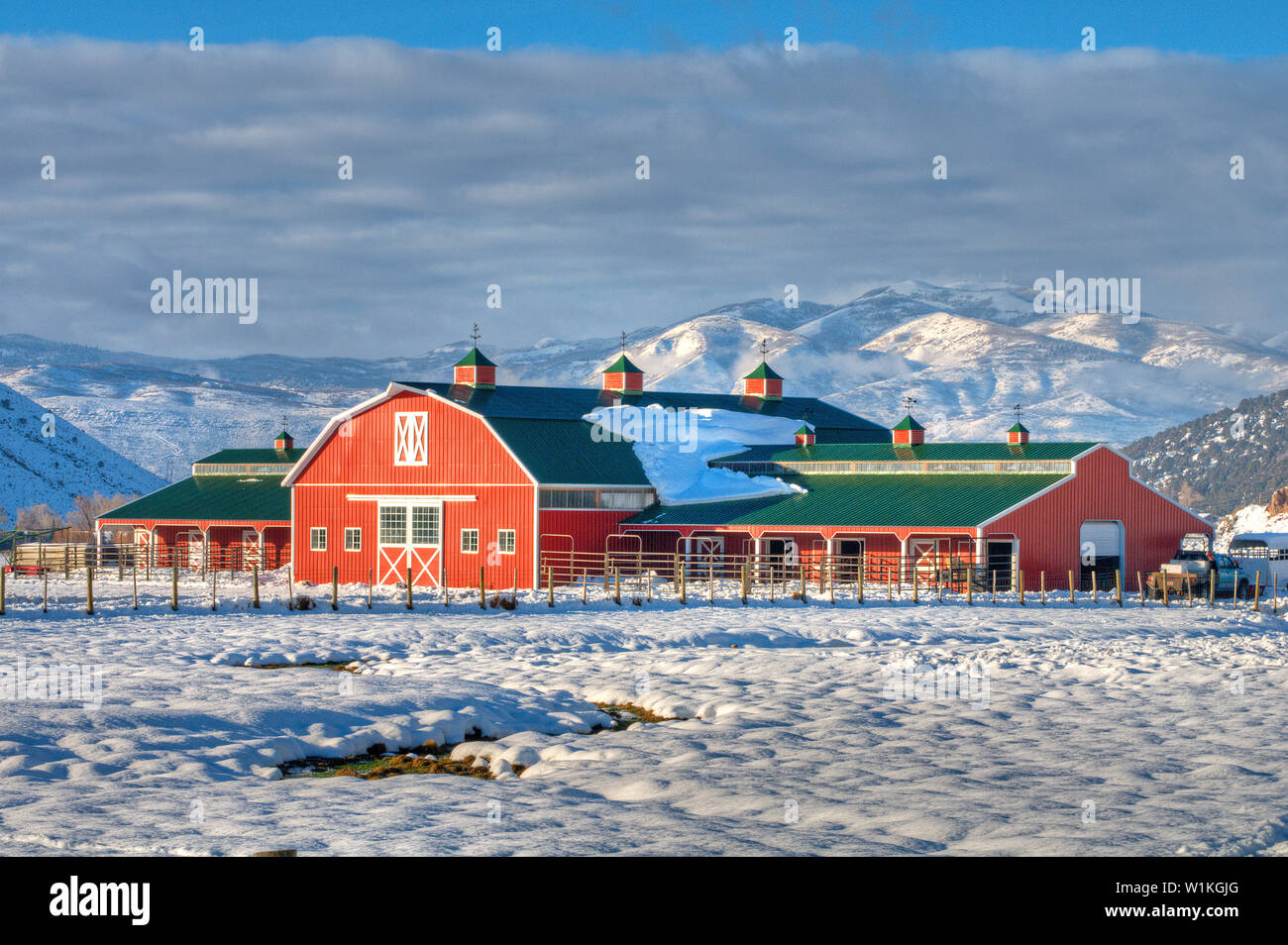 A Beautiful Red Barn Stands Out In A Snowy Mountain Landscape In