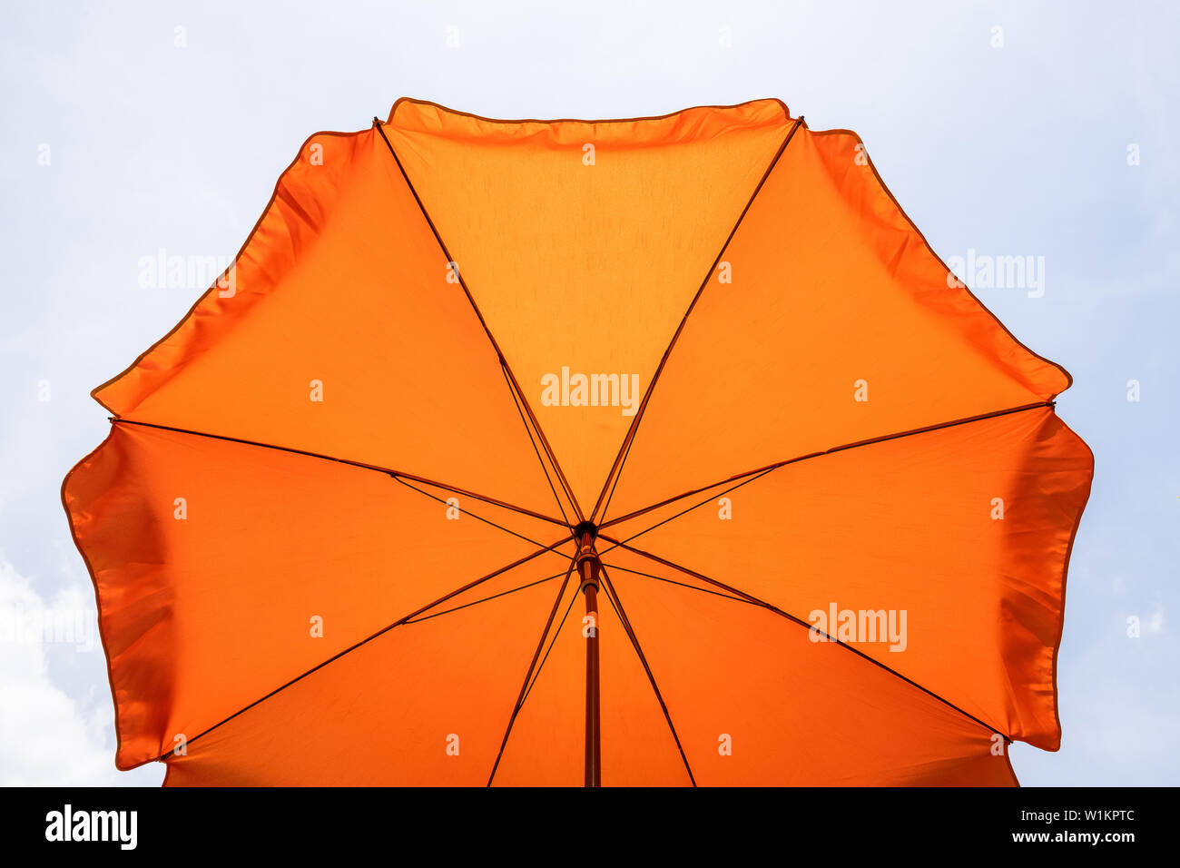 Description: Photo of a beach umbrella on the blue sky,Beach umbrella.One vibrant orange colored sunshade against vivid blue sky and white cloud. Stock Photo