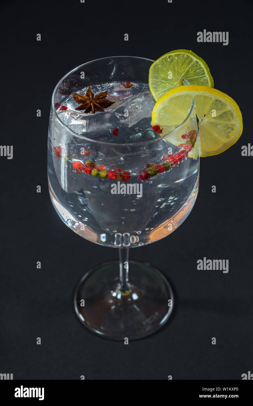 Gin Tonic in a glass cup with some slices of lime and lemon,pink pepper and anise on a black background Stock Photo
