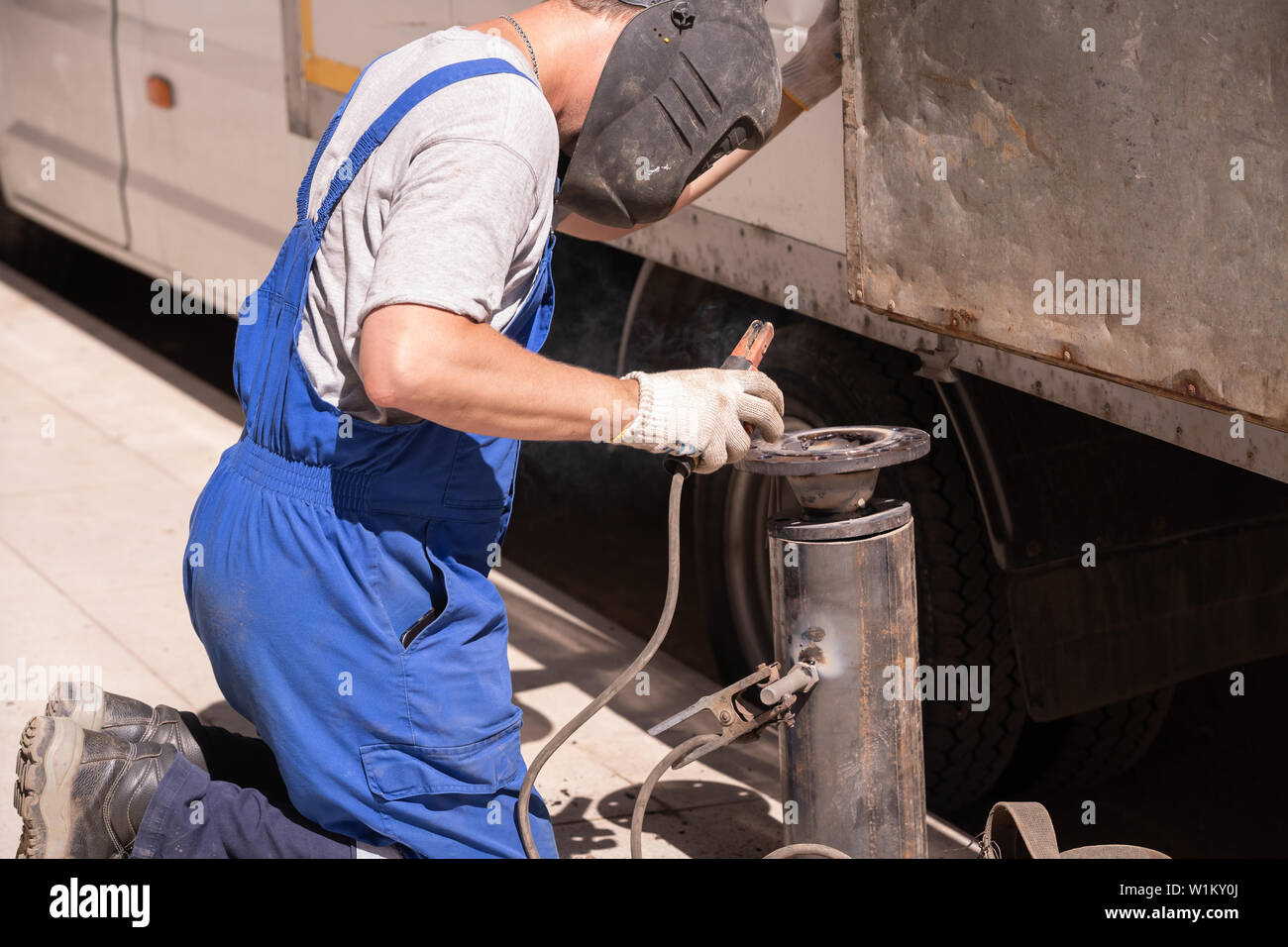 Description: welding work. A worker in overalls and a protective mask welds the flange to the pipe on the street. Repair work gorodskih communications Stock Photo