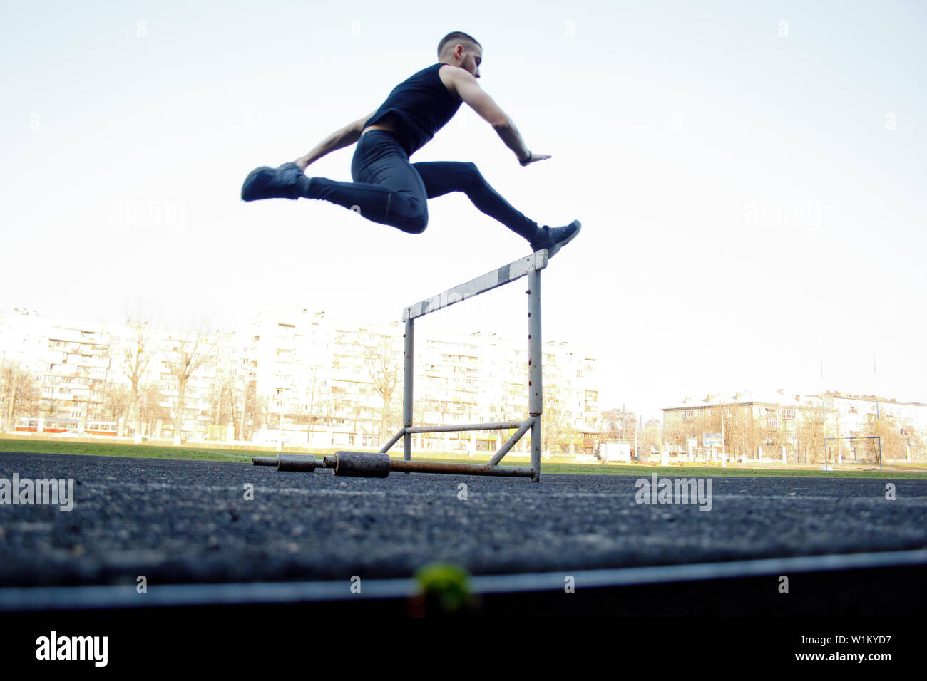 one caucasian male in a jump over a barrier. running on the stadium. Track and field runner in sport uniform in flight. energetic physical activities. Stock Photo