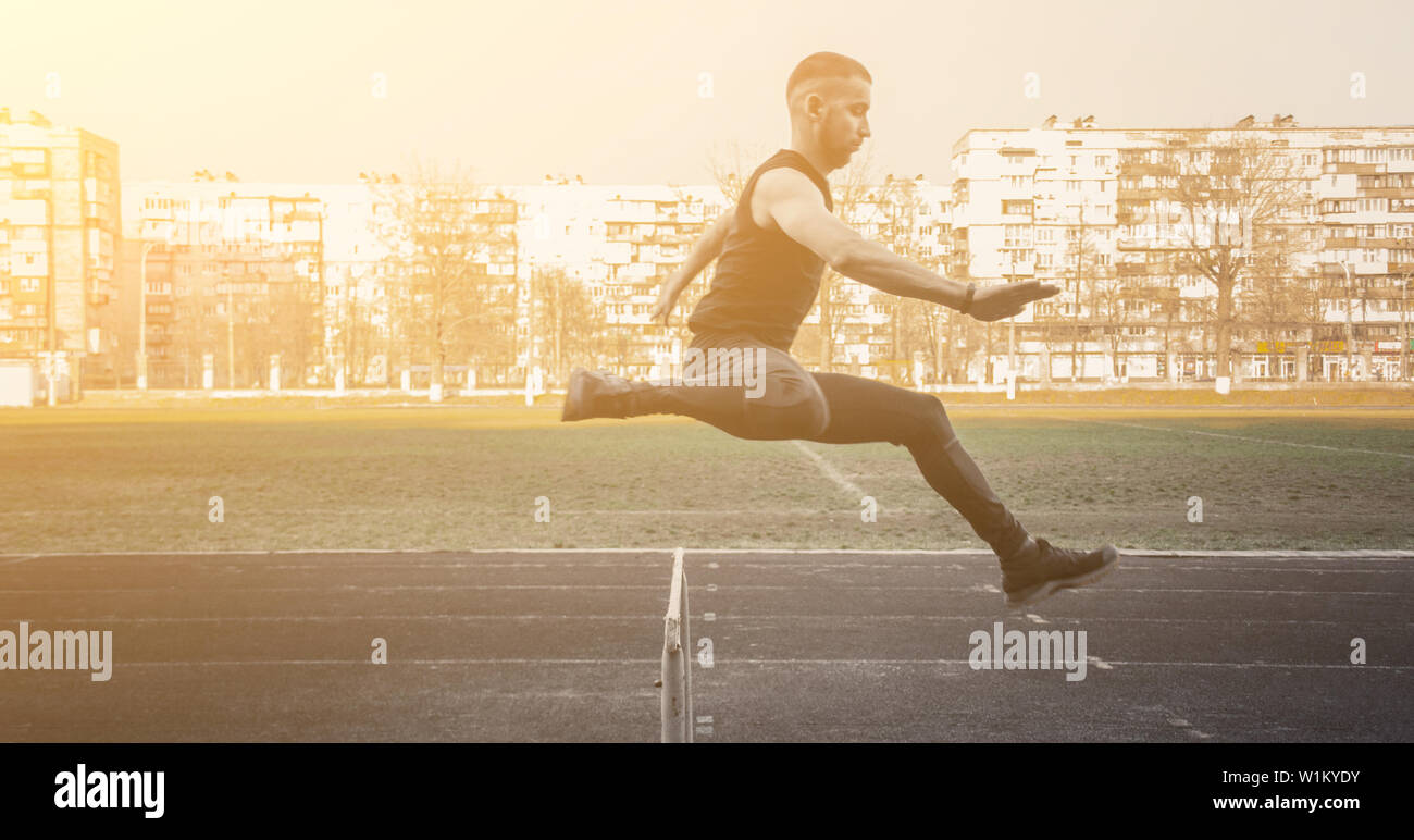 one caucasian male in a jump over a barrier. running on the stadium. Track and field runner in sport uniform in flight. energetic physical activities. Stock Photo