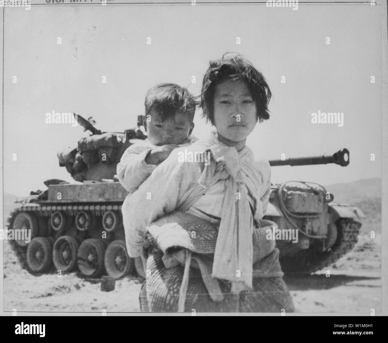 With her brother on her back a war weary Korean girl tiredly trudges by a stalled M-26 tank, at Haengju, Korea.; General notes:  Use War and Conflict Number 1485 when ordering a reproduction or requesting information about this image. Stock Photo