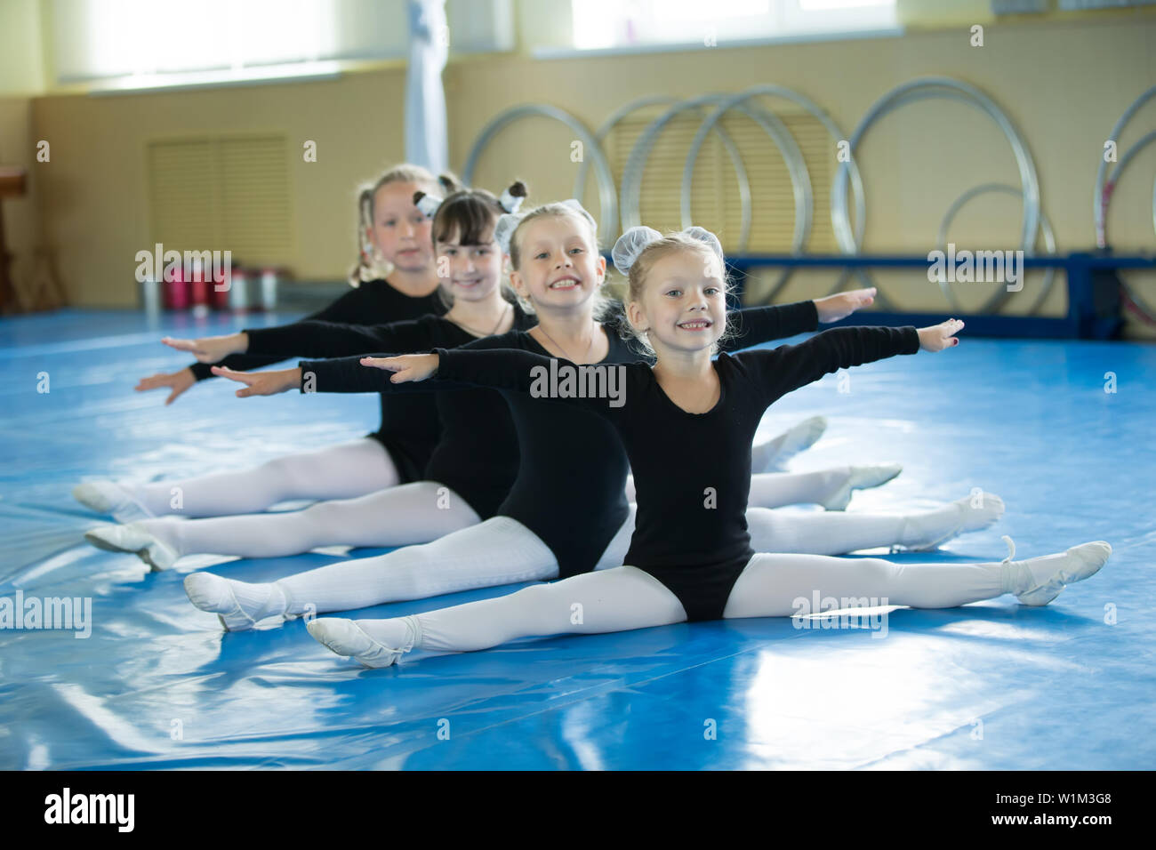 Little girls Gymnastics splits Little girls gymnasts sit on the splits. Children do physical exercise.  Young ballerinas.. Training of the initial group on gymnastics.Acrobatics  less Stock Photo - Alamy
