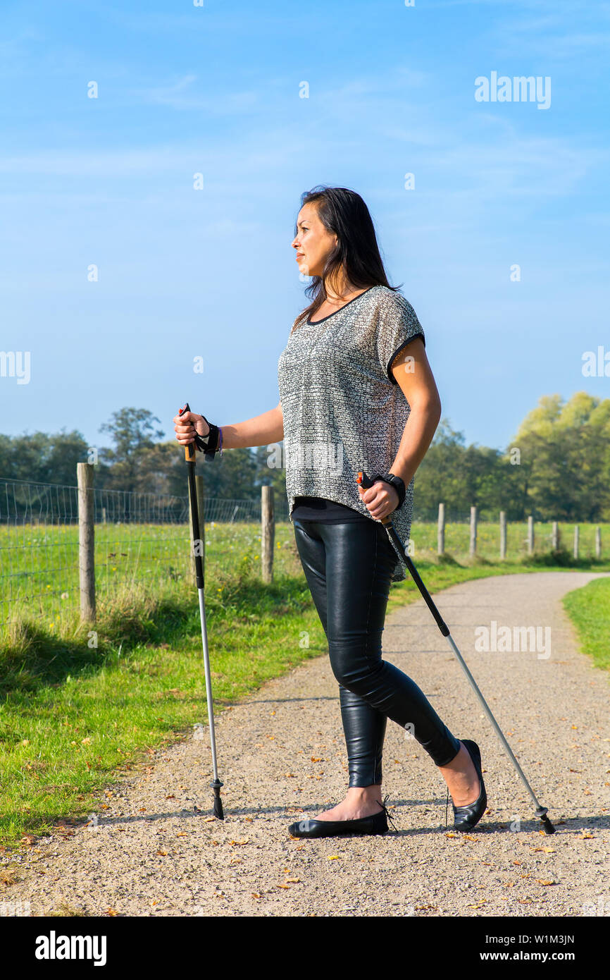 Young indian indonesian woman hiking with Nordic Walking sticks in dutch nature Stock Photo