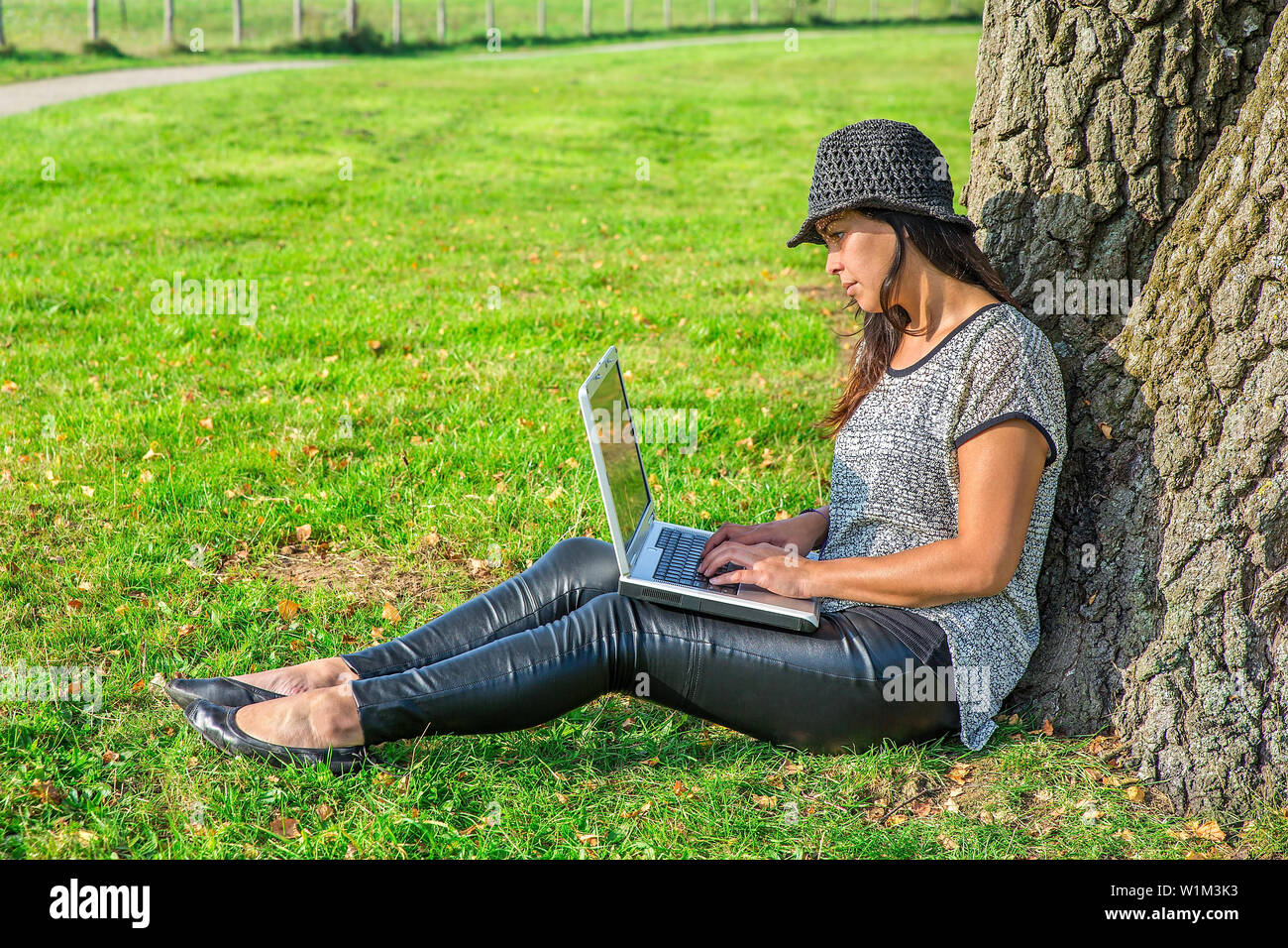 Young indian woman working with computer on lap at tree in nature Stock Photo
