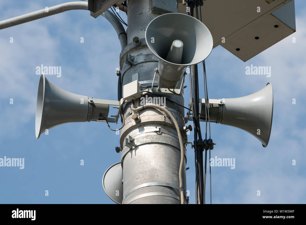 description: Three loudspeakers on pole against blue sky Stock Photo