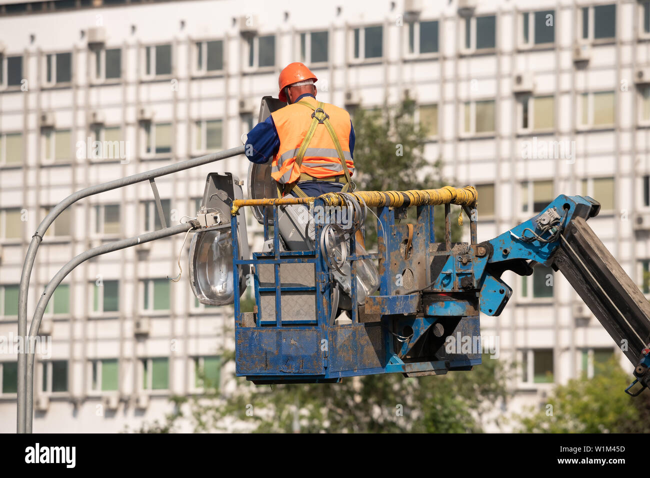 description: Worker in lift bucket during installation of metal pole with street lamp, street light pole with double head. Stock Photo
