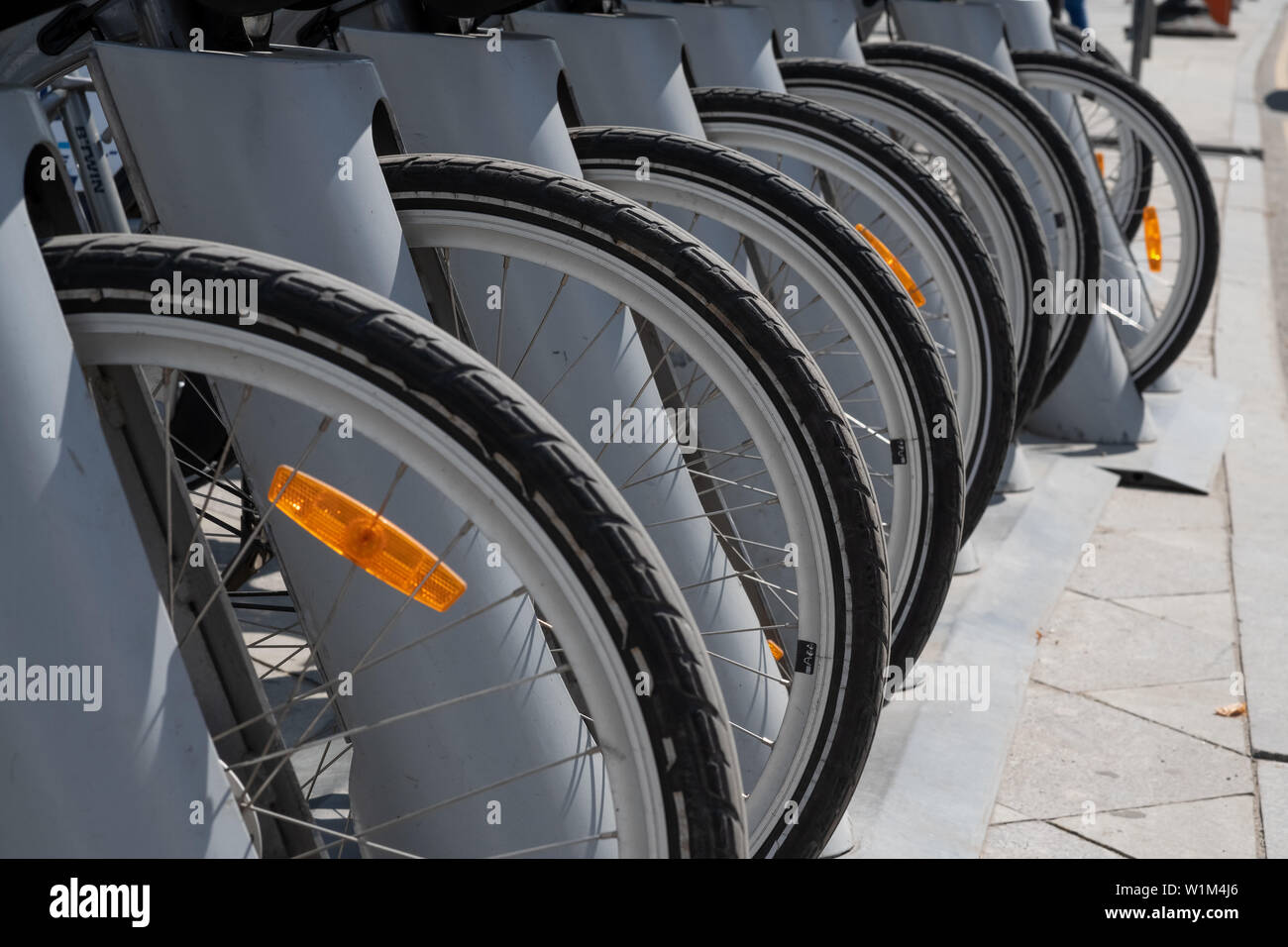 description: Wheels of parked bikes in the bike rental Parking lot.Bike hire pick up station.Rent a bike cheaply.Bicycle wheel in the perspective of t Stock Photo