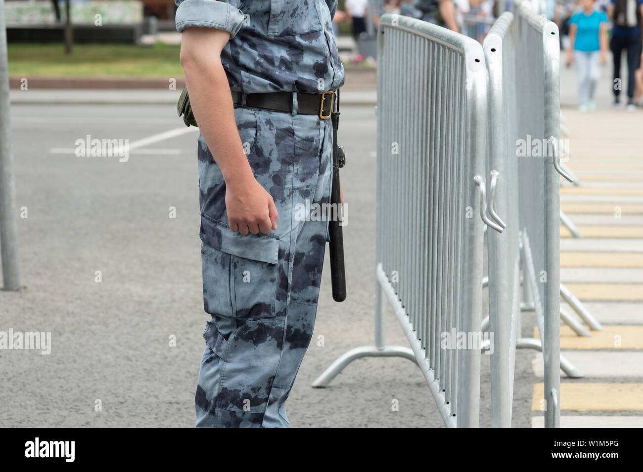 description: A policeman with a baton near the metal fence, close-up Stock Photo