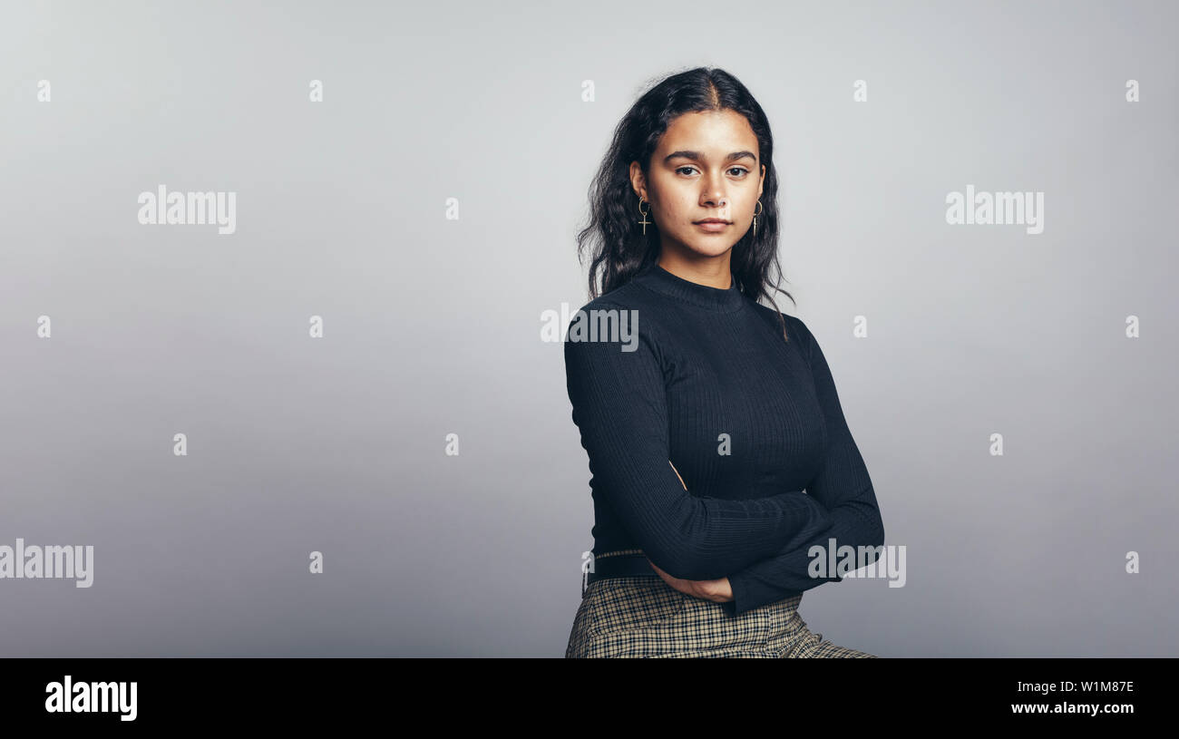 Portrait of young woman looking at camera. Woman sitting with her arms crossed against a grey background. Stock Photo