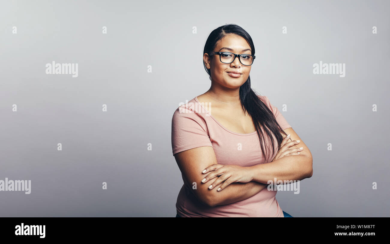 Portrait of young woman looking at camera. Woman in tshirt with her arms crossed against grey background. Stock Photo