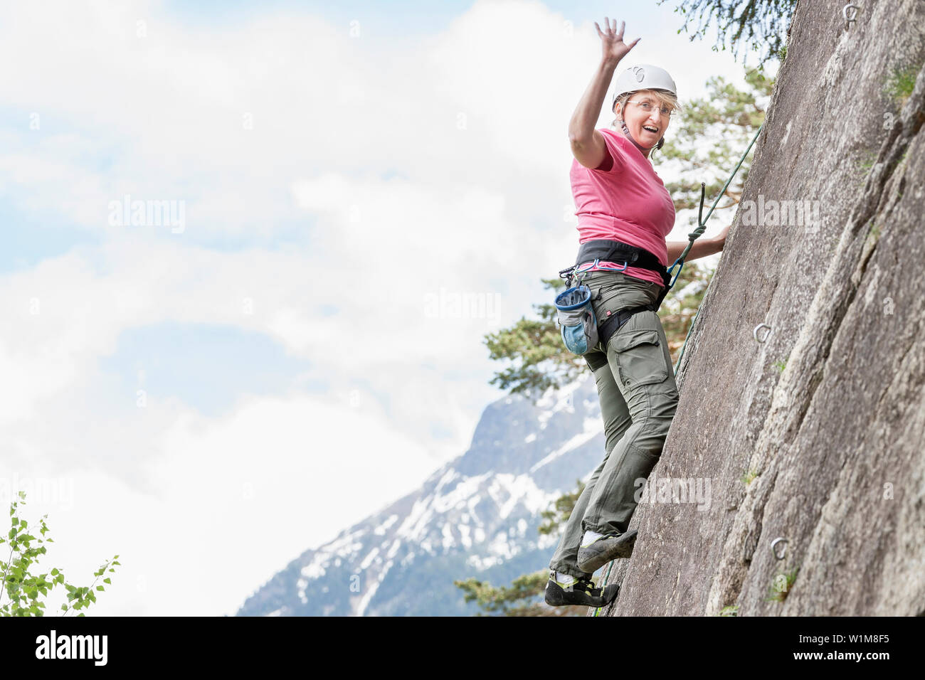 Female rock climber scaling a rock face and waving at Oberried climbing garden, Otztal, Tyrol, Austria Stock Photo